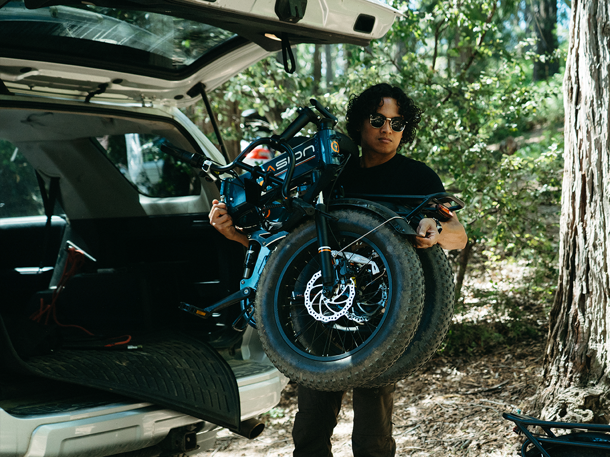 Person lifting a folded Jasion ebike beside an open car trunk