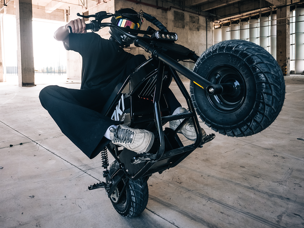 Helmeted rider performing a wheelie on a black Jasion Poki Electric Mini Bike inside a warehouse