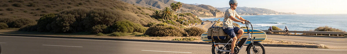 Jasion cargo electric bike rider carrying surfboard and bags along scenic coastal highway, versatile ebike for hauling gear