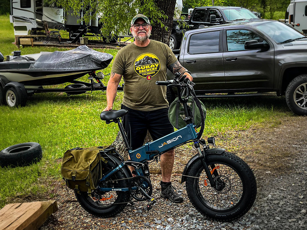 Rider beside a blue Jasion X-Hunter fat tire ebike with a rear pannier bag at a campsite