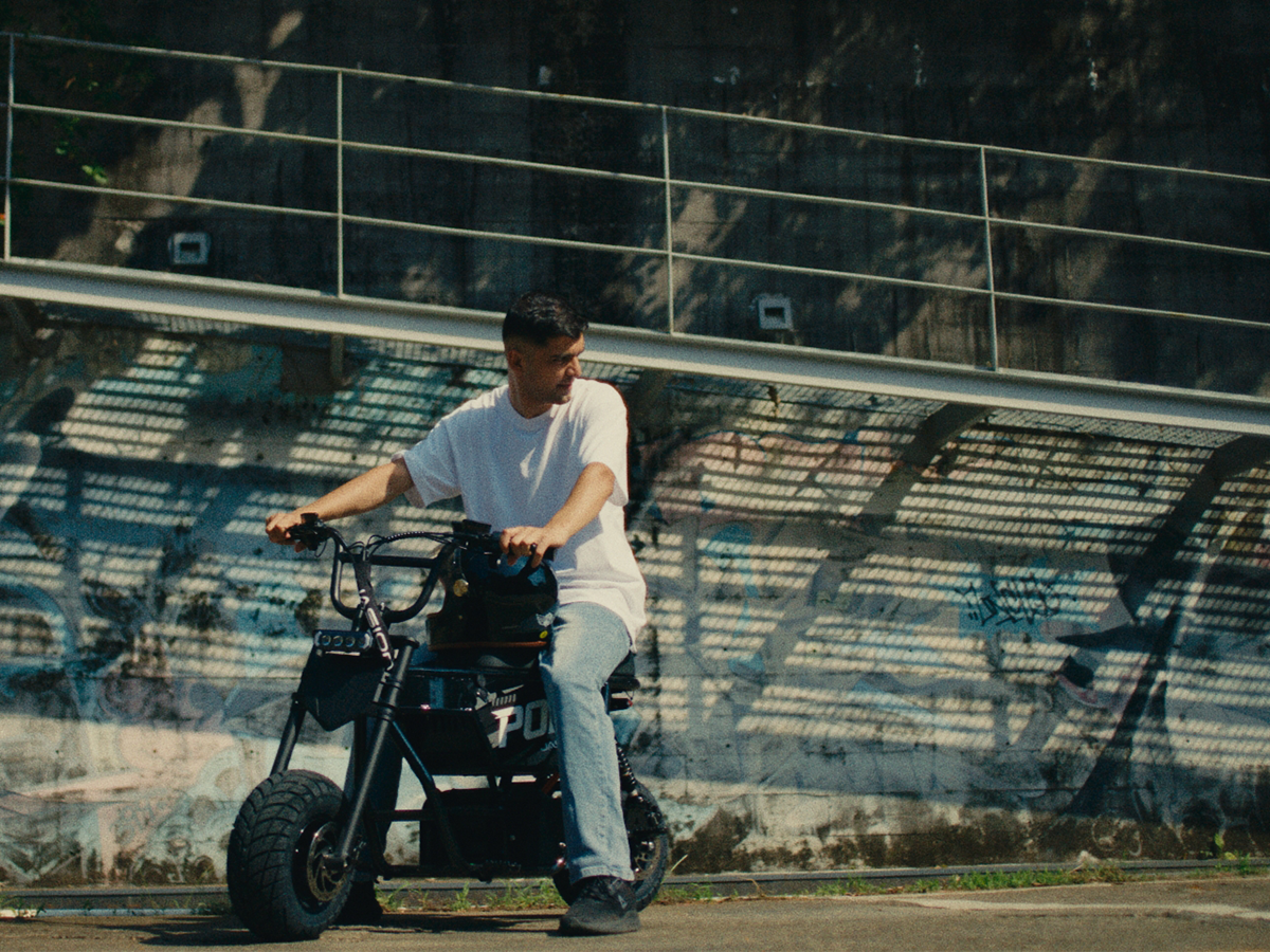 Rider seated on a black Jasion Poki Electric Mini Bike beside a graffiti-covered wall
