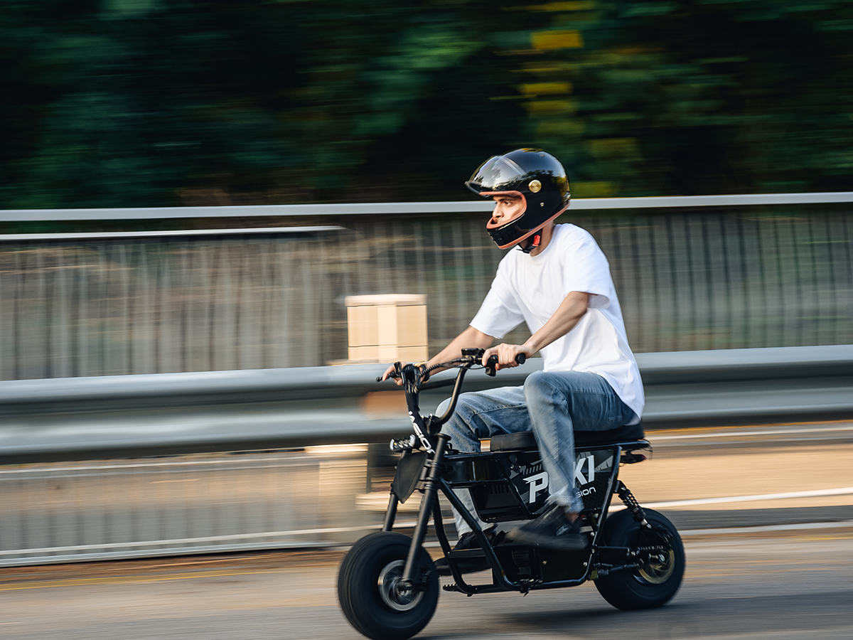 Helmeted rider riding a black Jasion Poki Electric Mini Bike alongside a metal guardrail